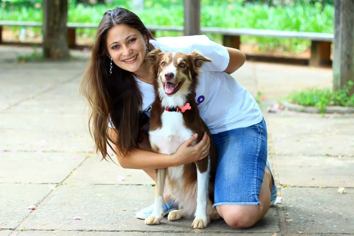 Adestradora Fernanda Conrado abraçada à cachorra Catarina em um parque
